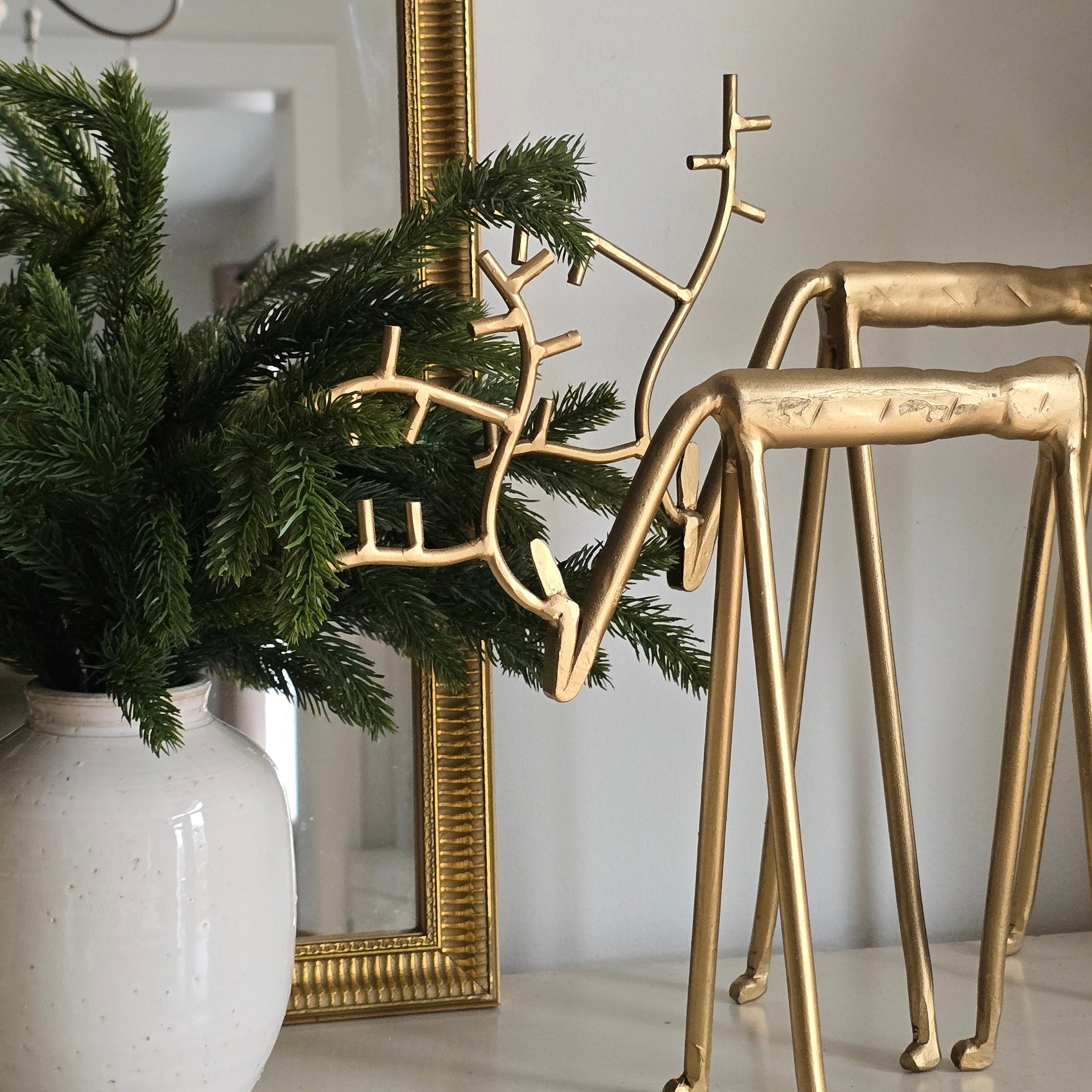 Gold decorative branch on a small Christmas tree with a white vase and mirror in the background.