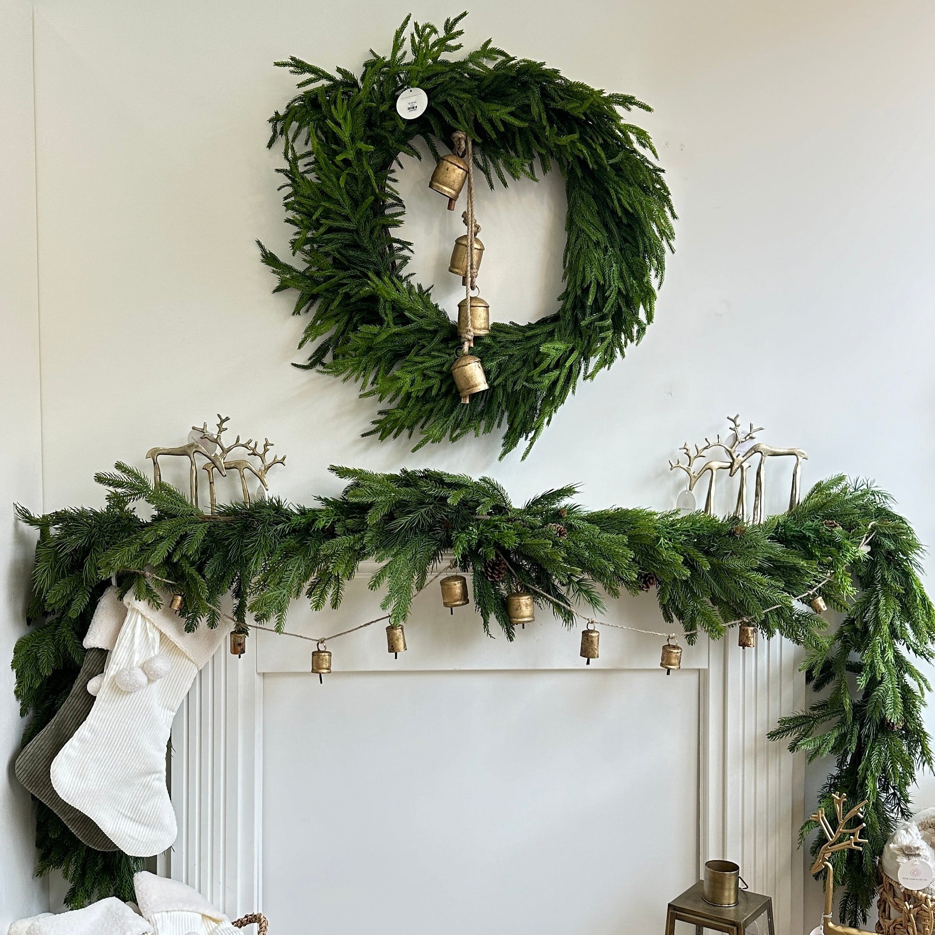 Decorative Christmas mantel with wreath, garland, and stockings against a white wall.