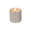 Candle in a ribbed concrete holder on a wooden surface