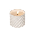White textured candle with a lit flame on a wooden surface
