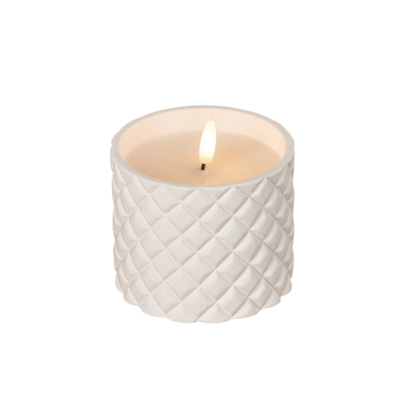 White textured candle with a lit flame on a wooden surface