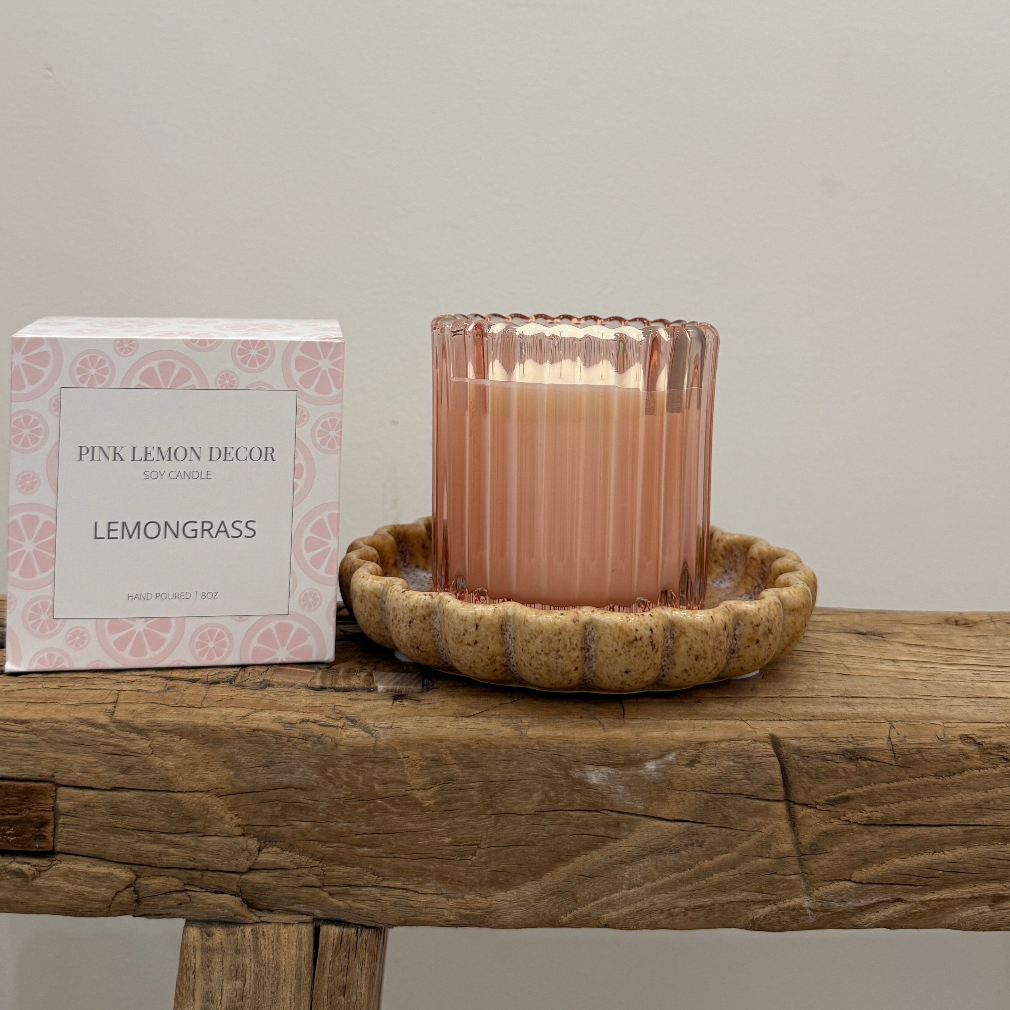 Pink candle in a ribbed glass holder on a wooden surface with a white box labeled 'Pink Lemon Decor' in the background.