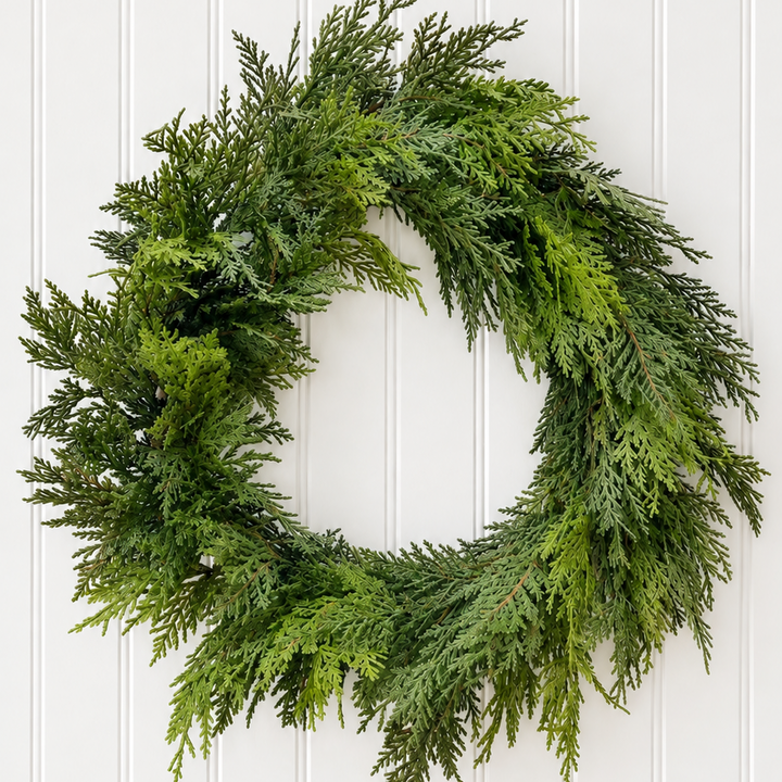 A lush green artificial evergreen wreath hanging on a white vertical-paneled wall.