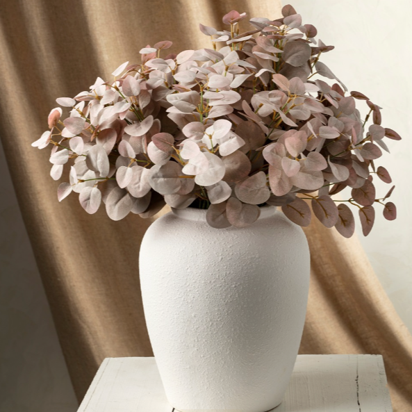 White vase with pink flowers against a beige curtain background