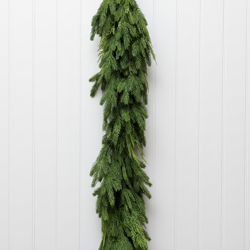 A long green evergreen garland hangs vertically against a white painted brick wall.