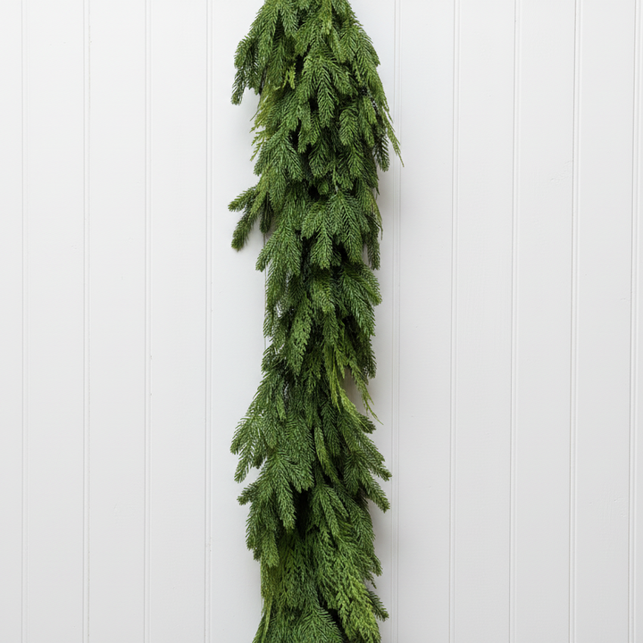 A long green evergreen garland hangs vertically against a white painted brick wall.