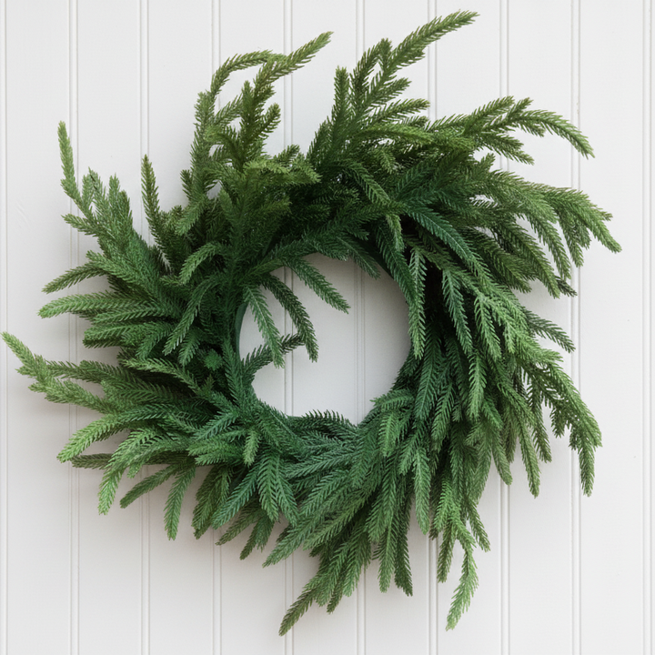 A green artificial pine or fir-style wreath with dense needle-like branches, laid flat on a rustic wooden plank surface.