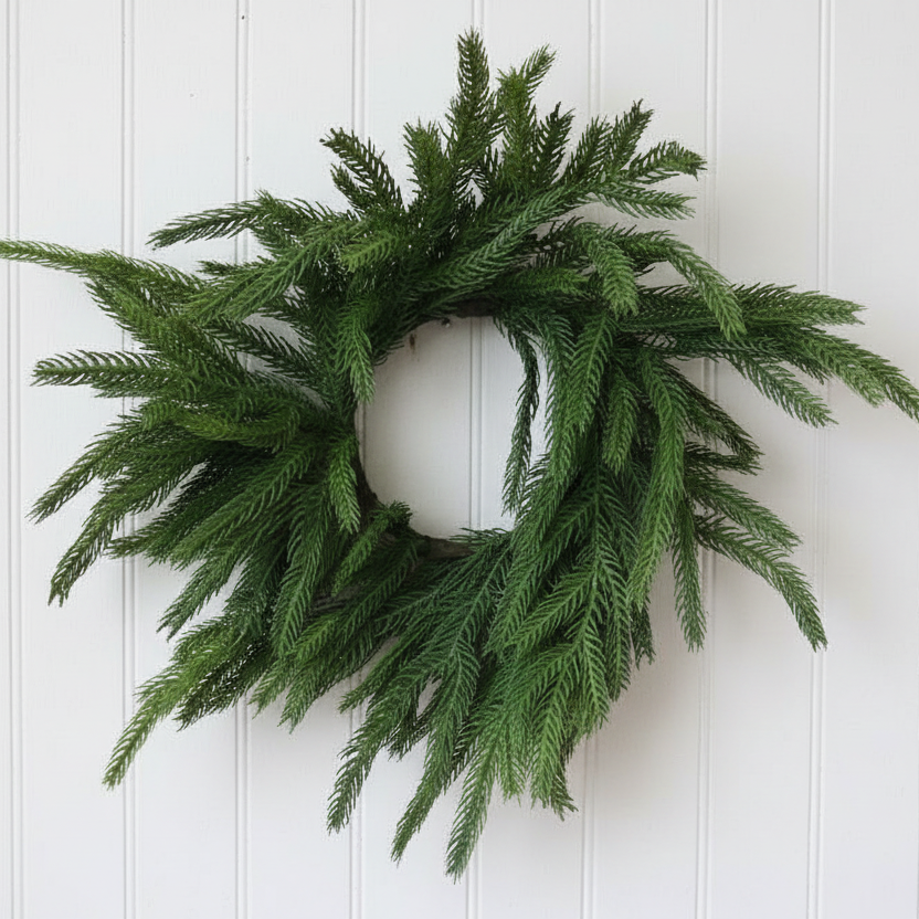 A green artificial pine wreath with realistic needle-like branches, displayed against a rustic light brown wooden plank background.