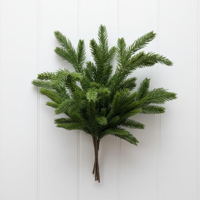 A bundled artificial green pine or fir branch arrangement tied with a small piece of twine, displayed against a white painted brick wall.