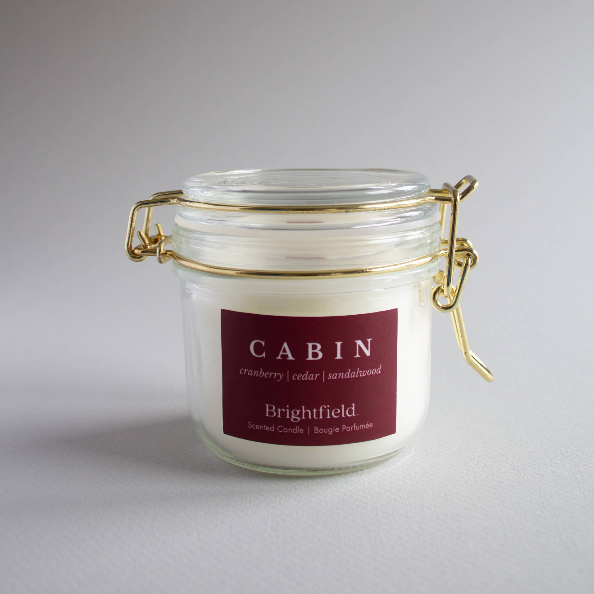 Glass jar candle with a maroon label on a gray background