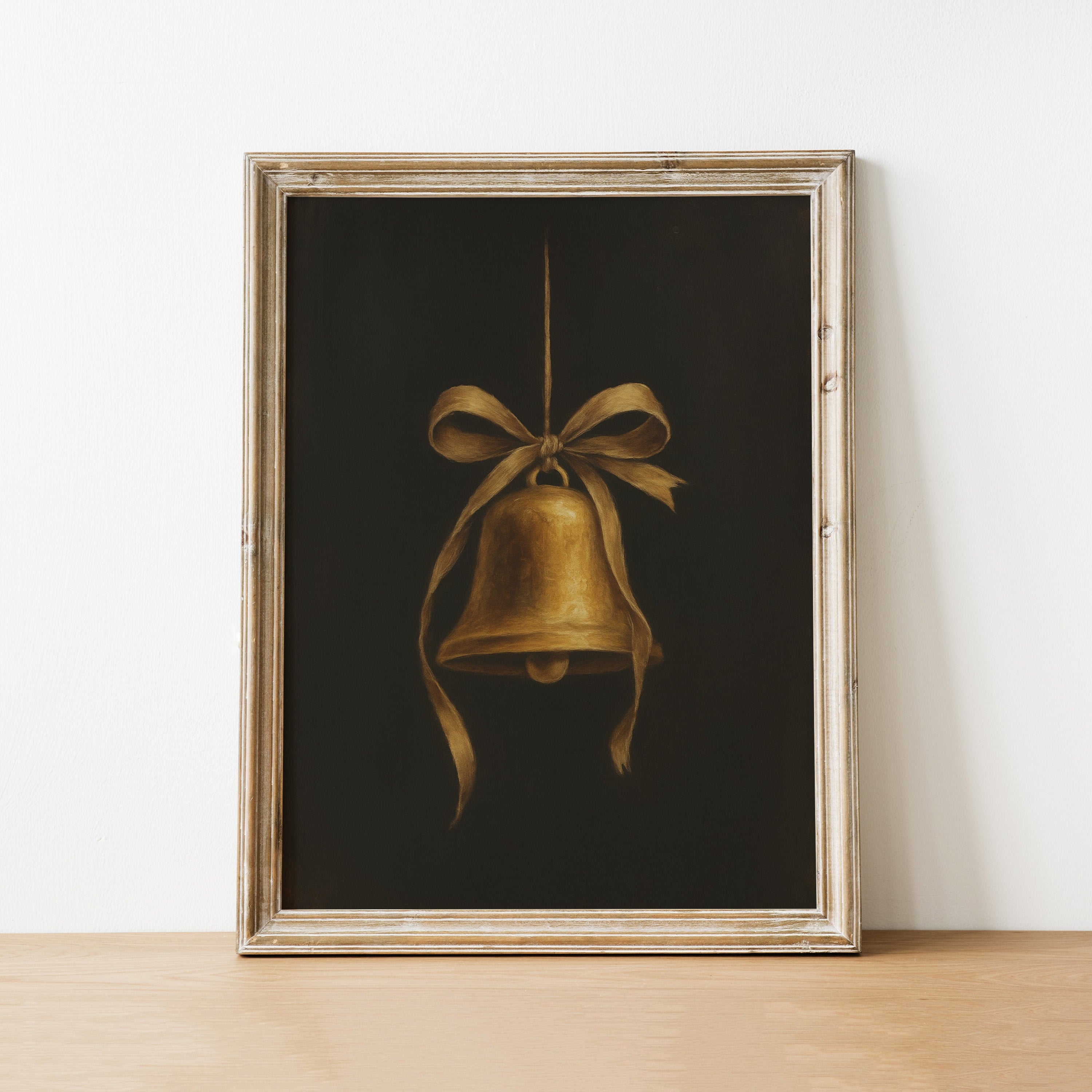 Framed artwork of a gold bell with a bow on a white wall.