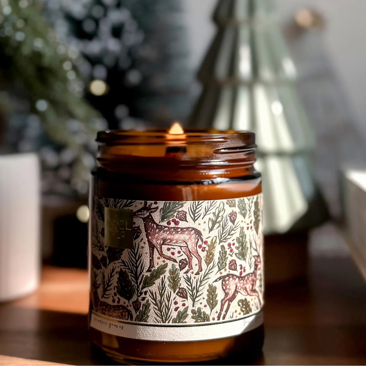 Candle in a decorative jar with a Christmas tree in the background